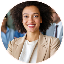 A headshot, enclosed in a circular frame, of a confident, smiling African-American woman with curly hair, wearing a beige blazer over a white top. She is looking directly at the camera, with the blurred figures of colleagues in business attire visible in the background.